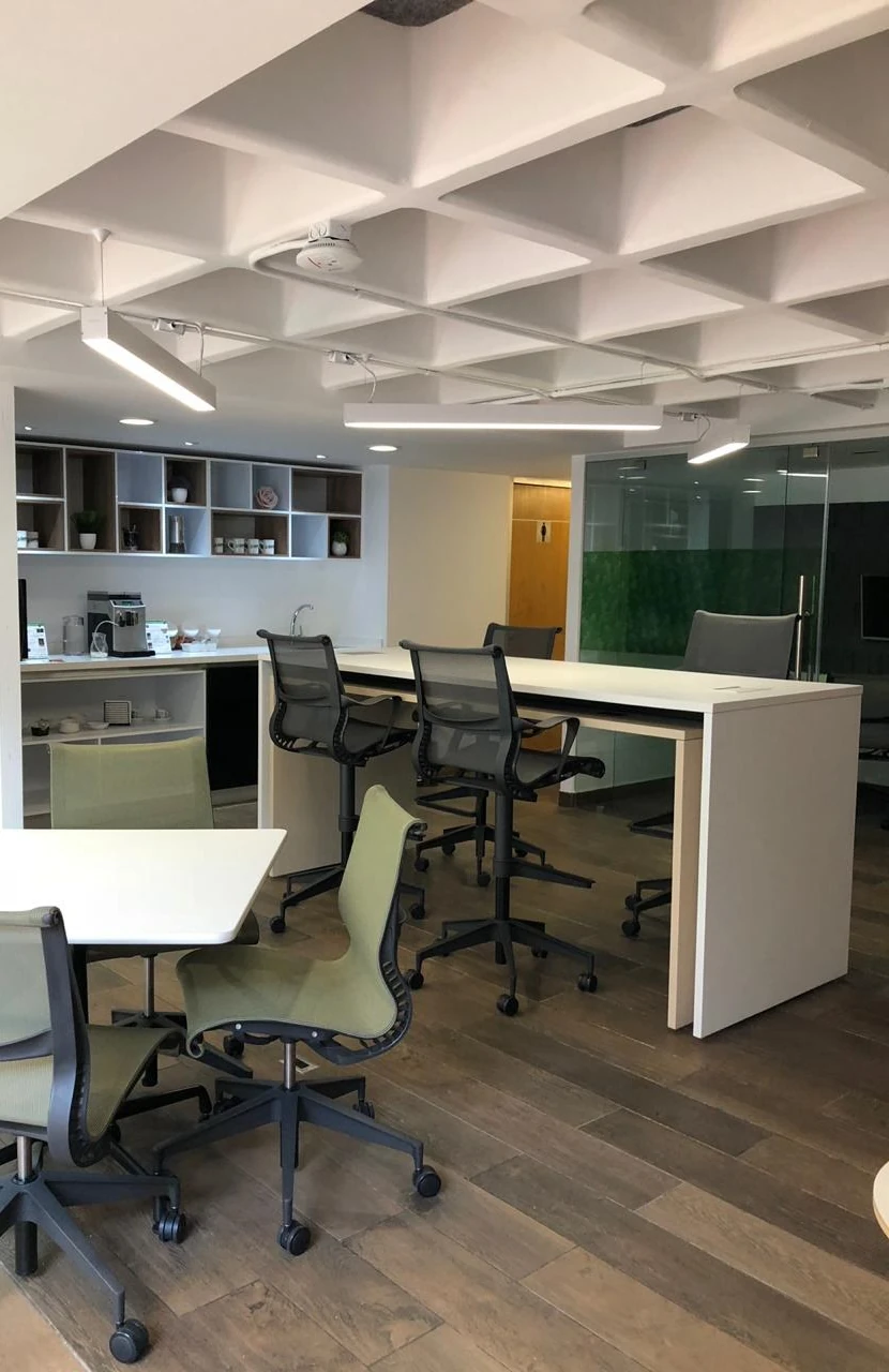 Interior de oficina con techo de casetones, mesas altas y sillas verdes
